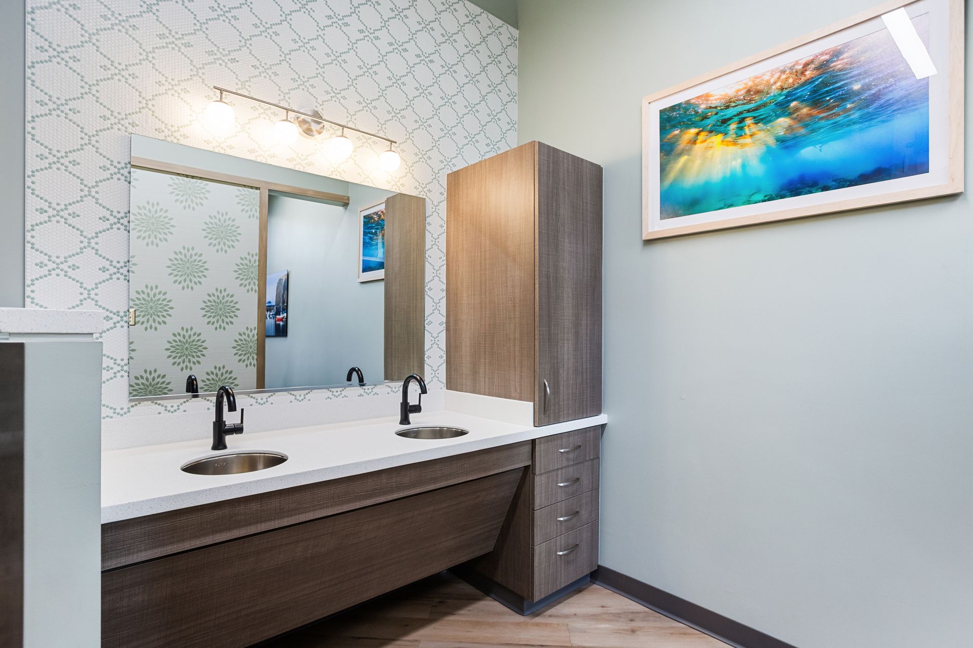 Modern bathroom with double sinks, gray cabinets, patterned backsplash, and abstract artwork.