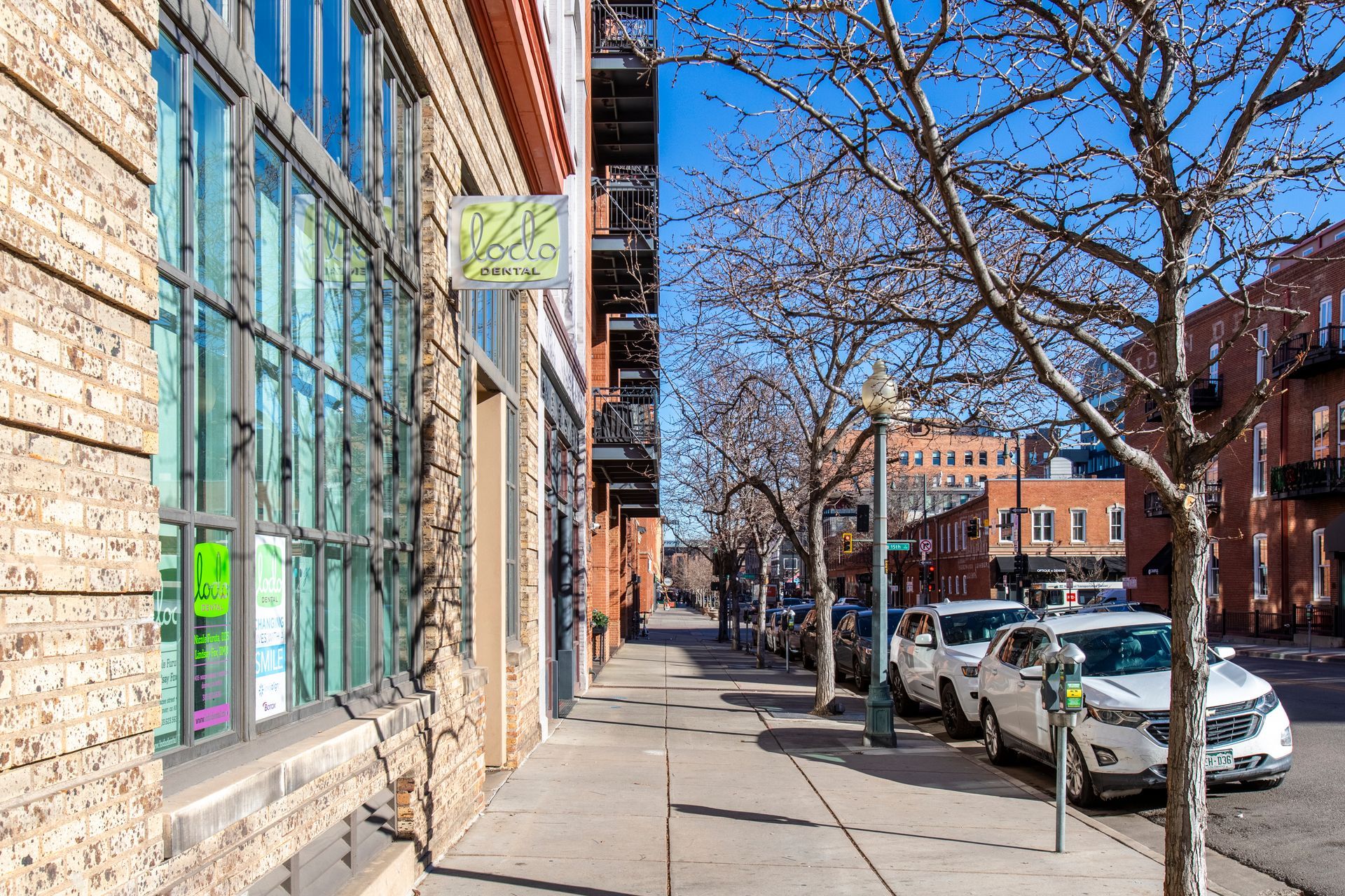 Street view of brick buildings with sidewalk and parked cars on a sunny day.