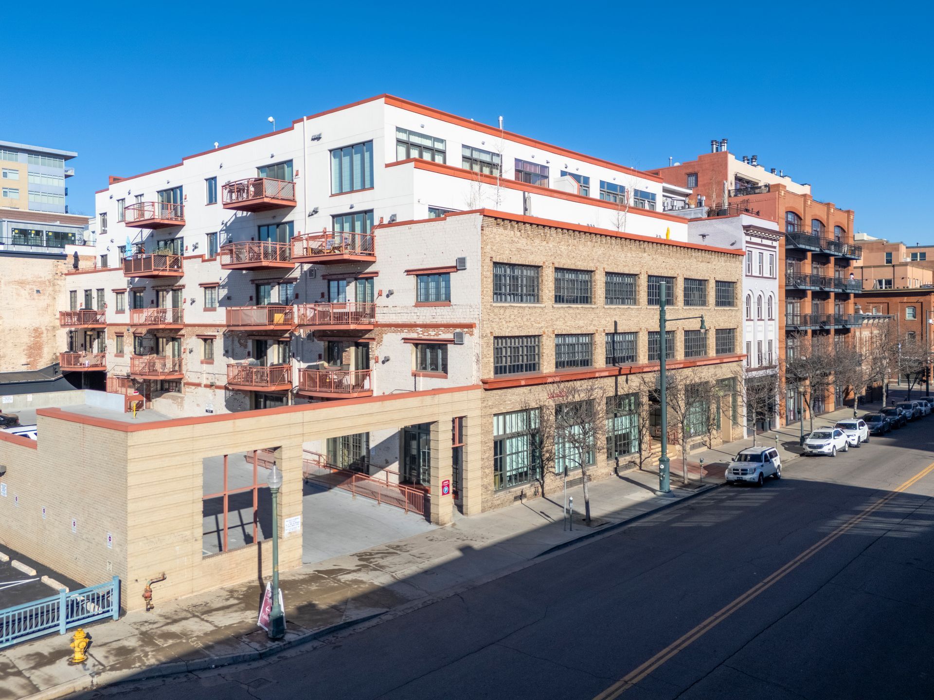 Multi-story brick building with balconies and storefronts on a city street under a blue sky.