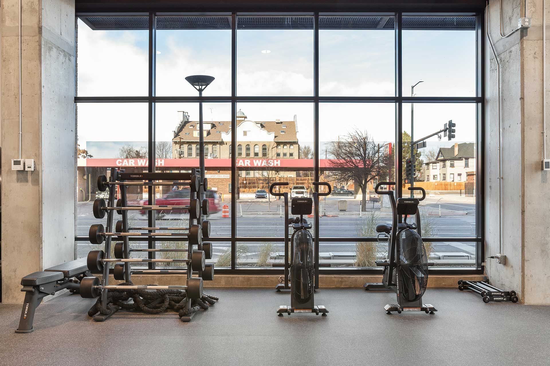 gym with weights, stationary bikes, and a large window overlooking a street with buildings