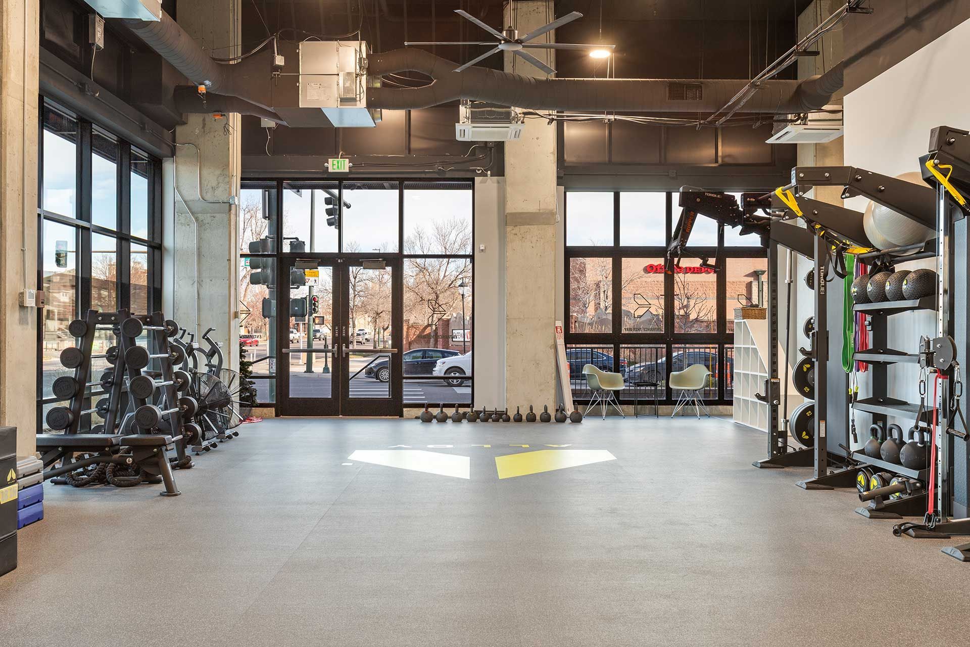 gym interior with weights, machines, and large windows overlooking a street scene