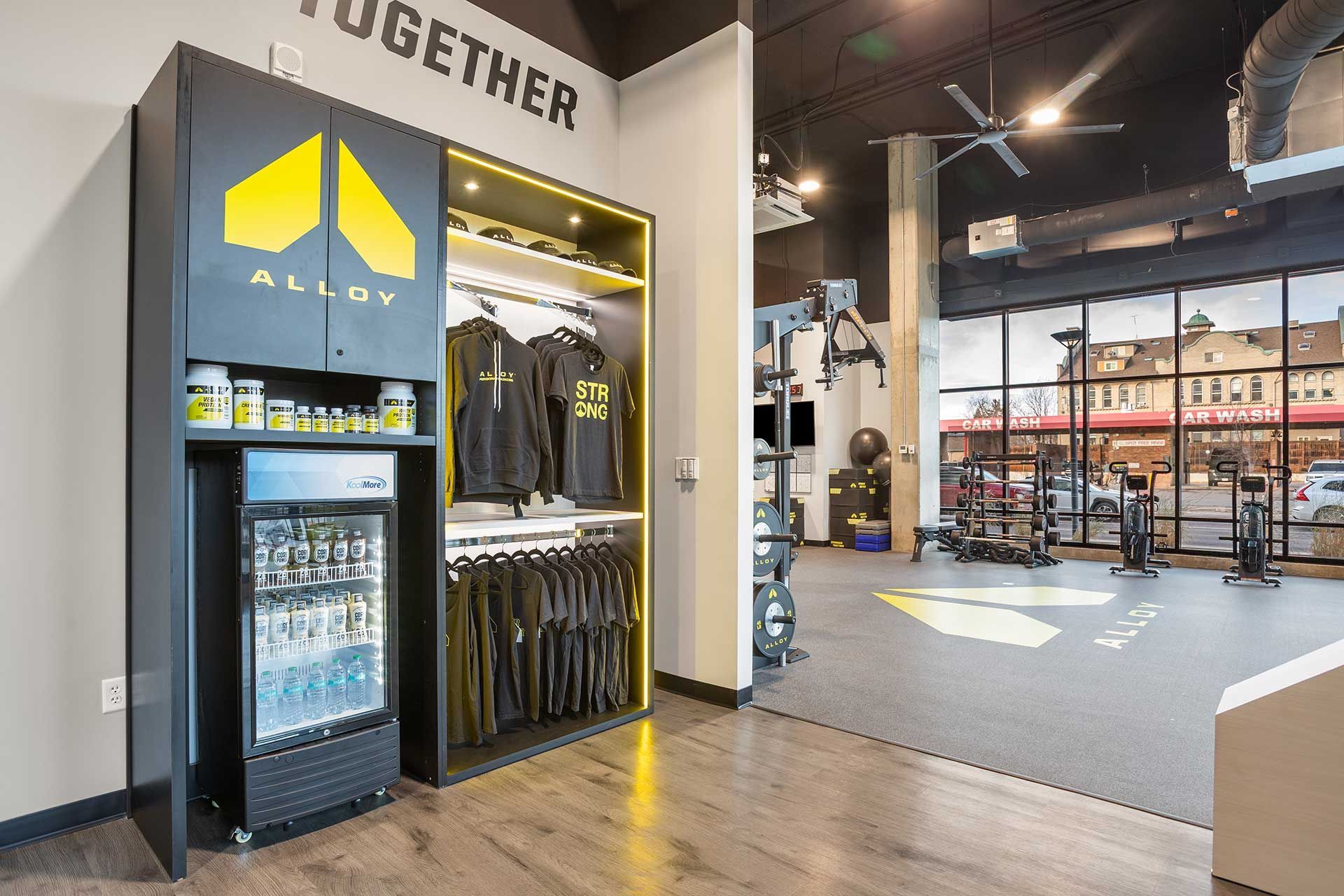 gym interior with black cabinet, t-shirts, and refrigerator, with gym equipment and a large window