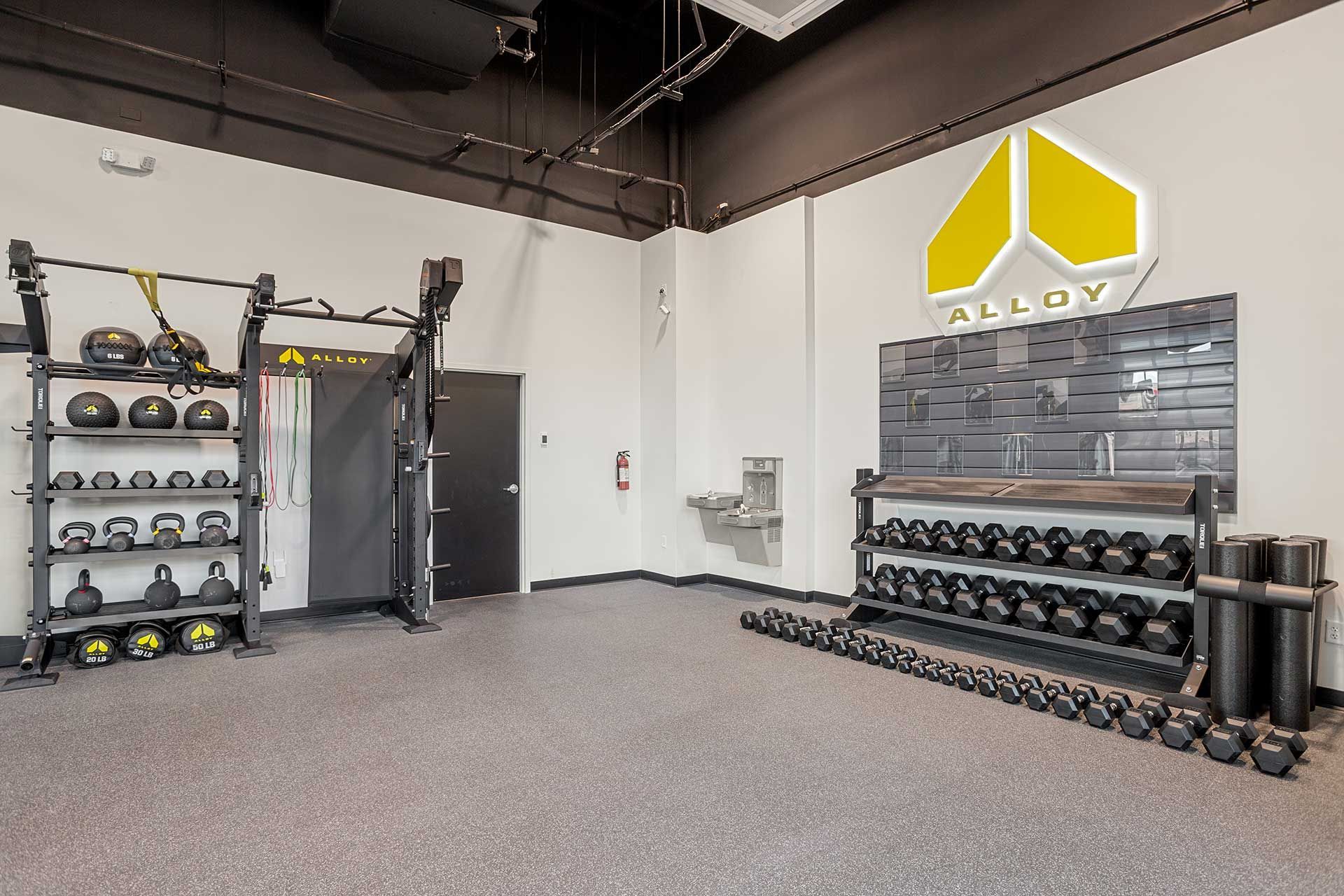 gym interior with weight racks, dumbbells, and workout equipment, gray and yellow logo on wall