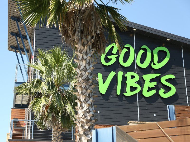 A building with a sign that says `` good vibes '' next to a palm tree.