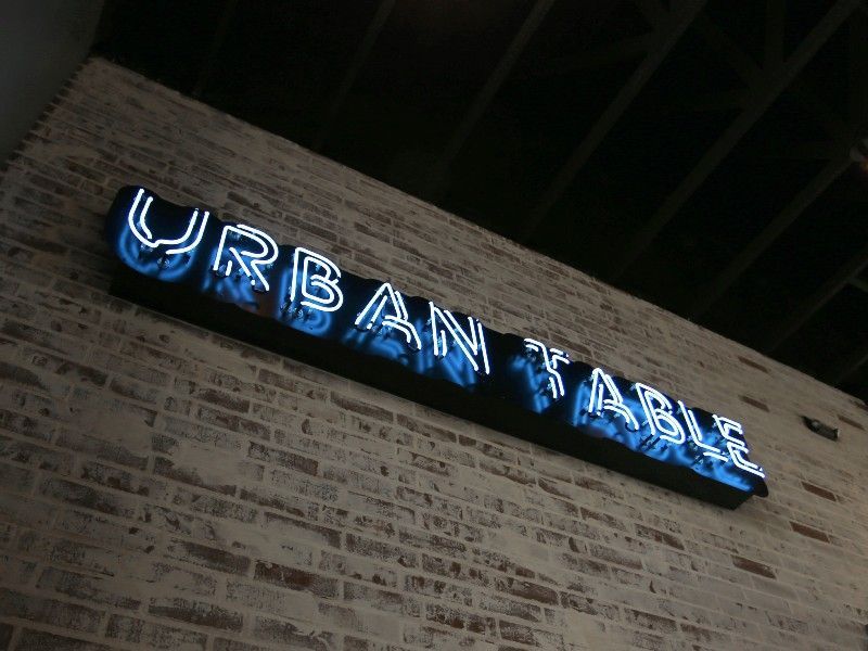 A neon sign that says urban table on a brick wall