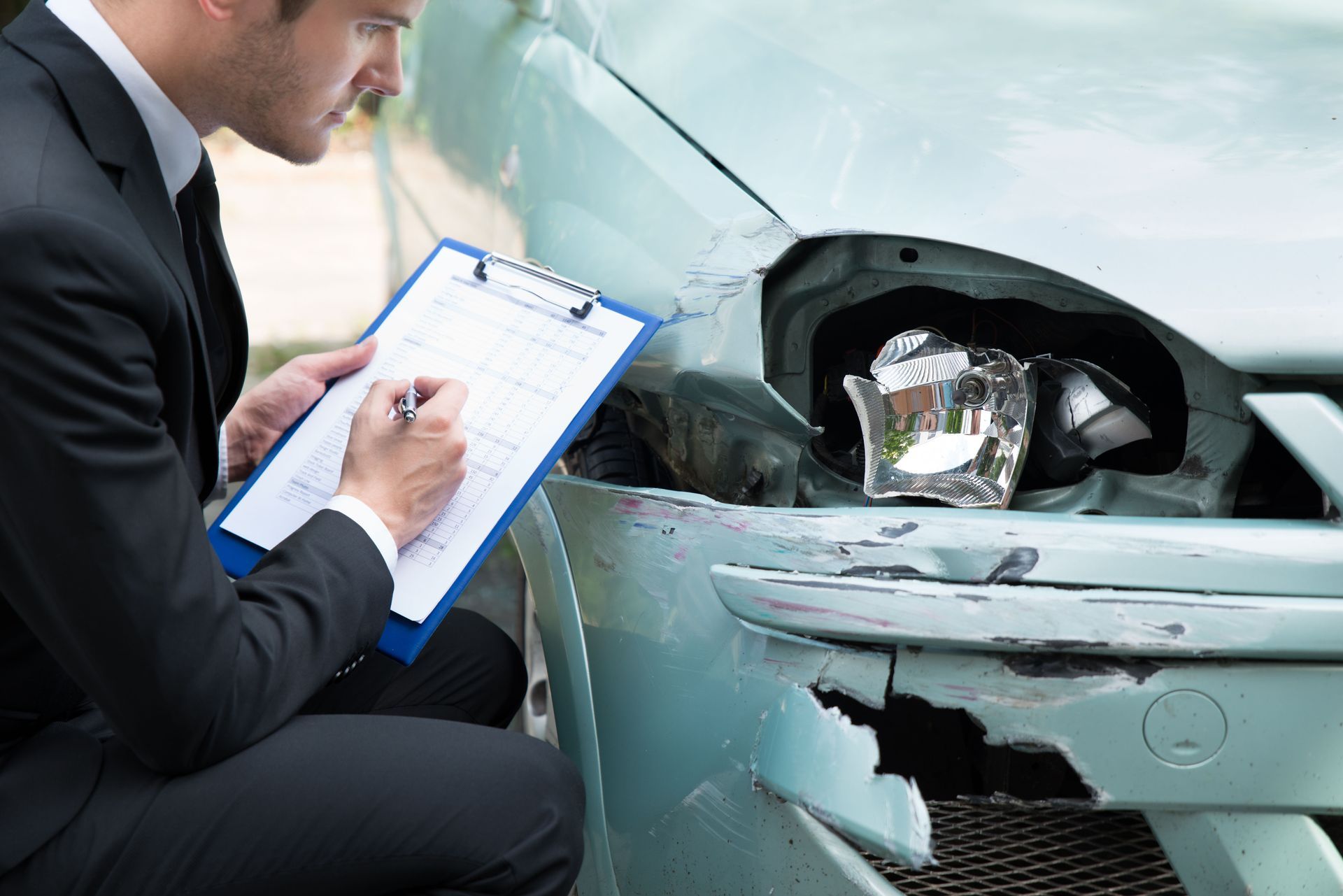 Insurance adjuster inspecting a damaged car, taking notes on a clipboard.