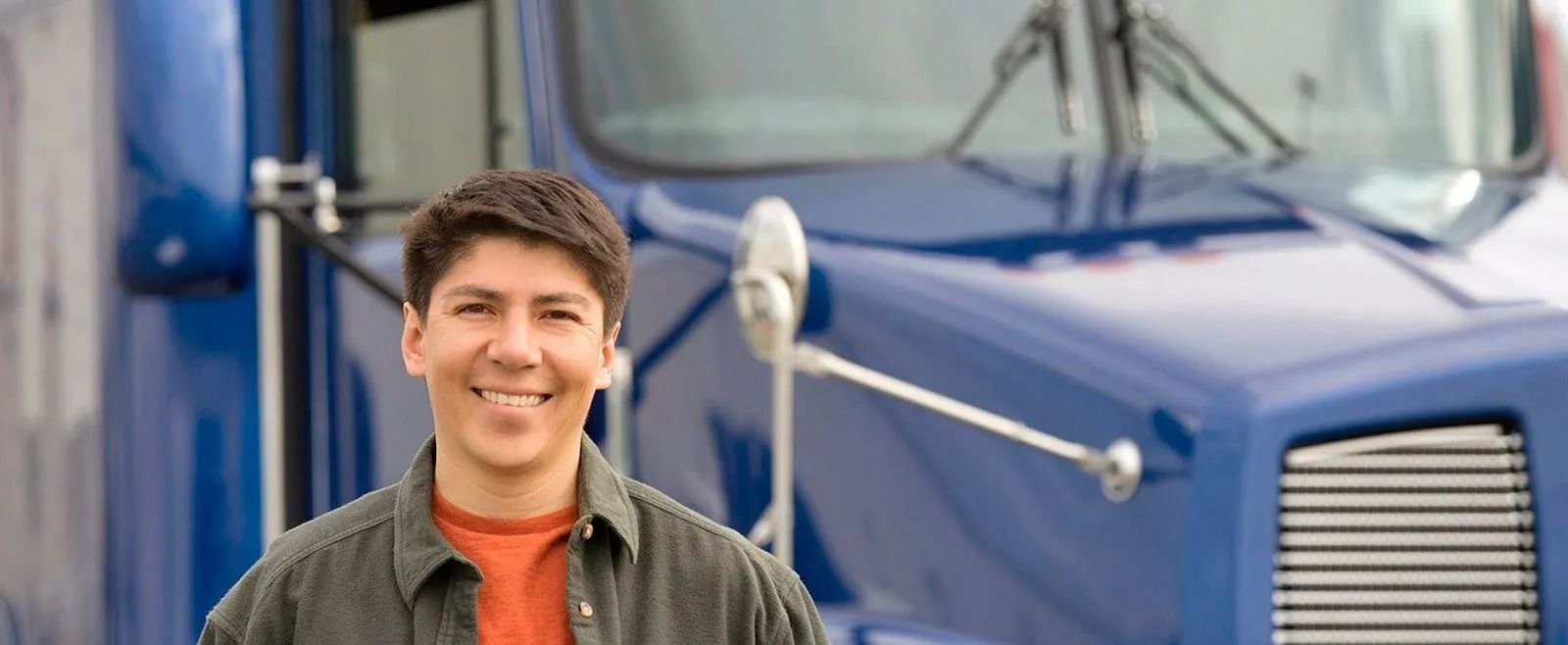 Man smiling in front of a blue semi-truck.