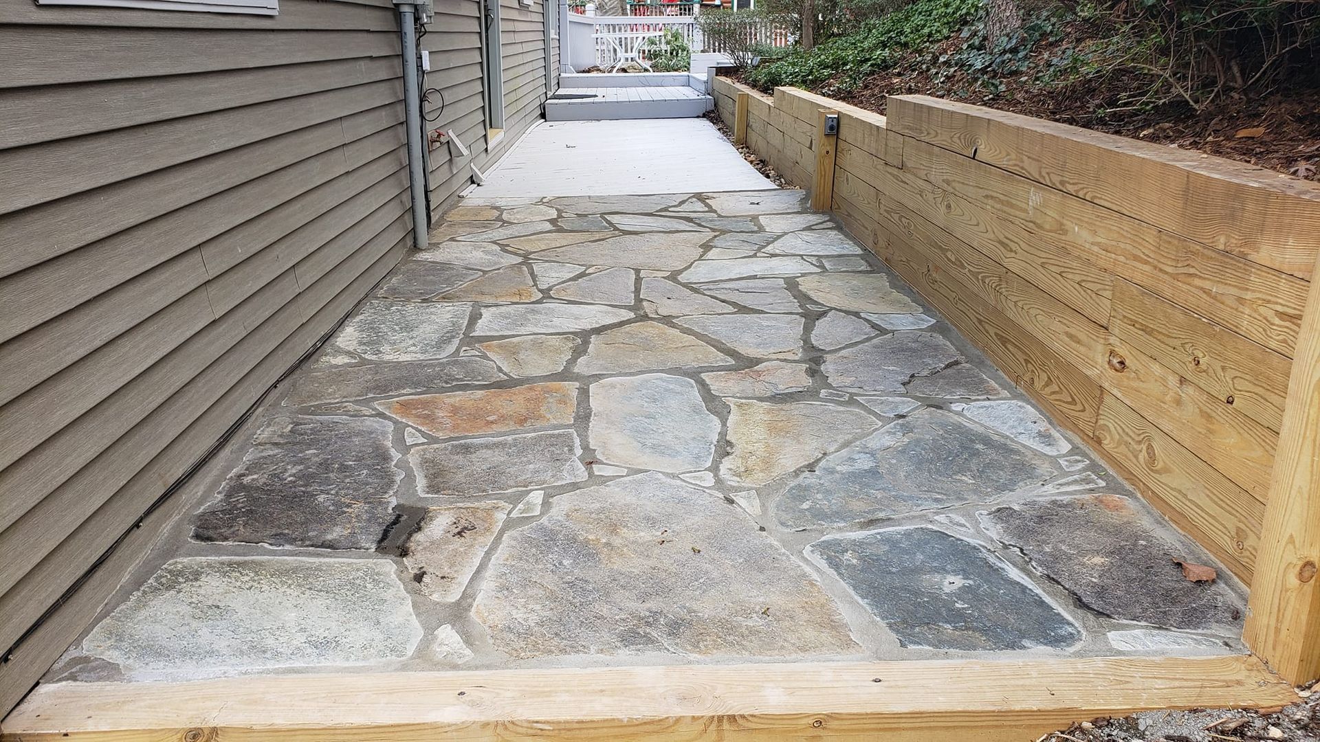 A stone walkway leading to a house next to a wooden wall