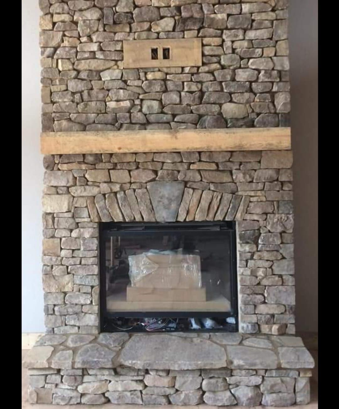 A stone fireplace with a wooden mantle in a living room