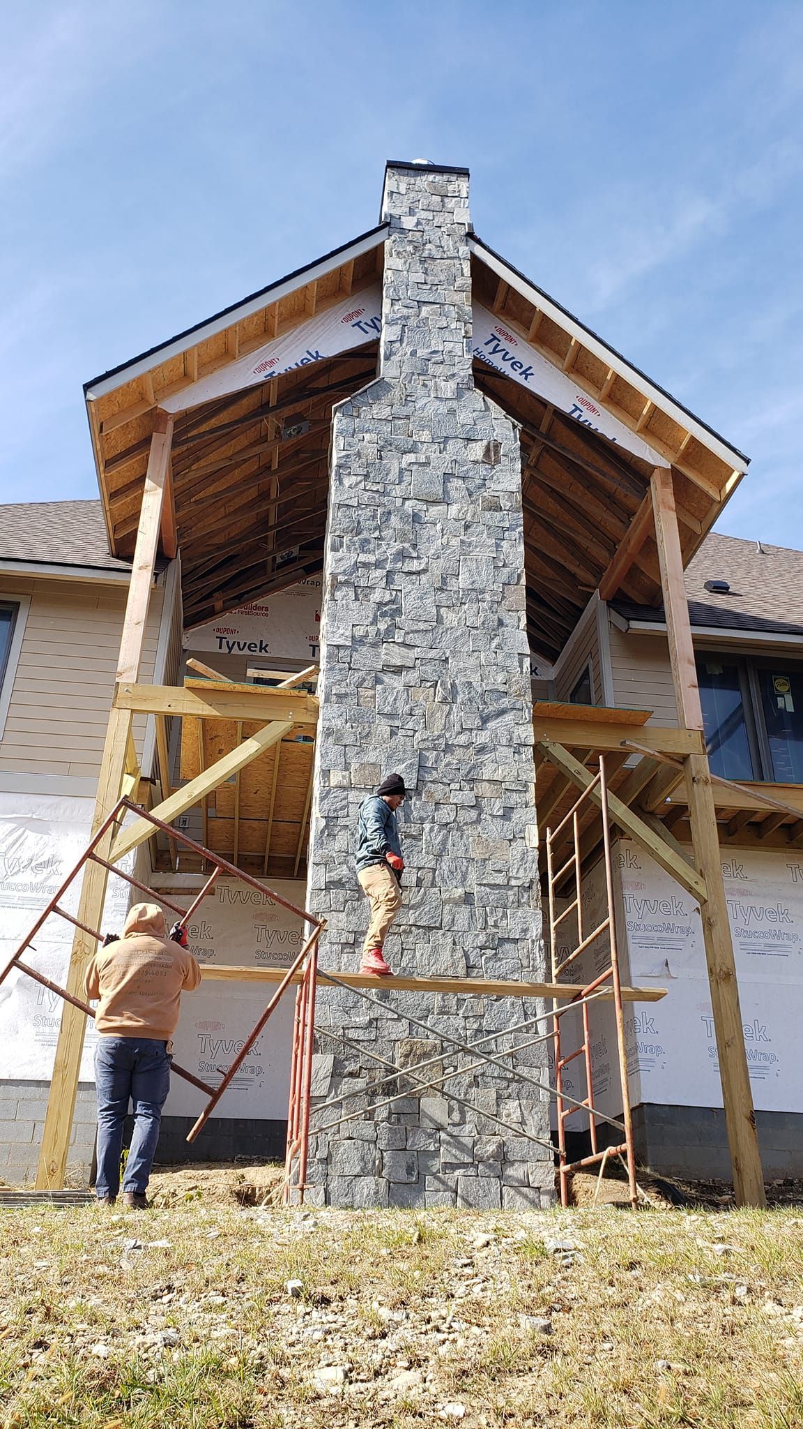 A large stone fireplace is being built on the side of a house