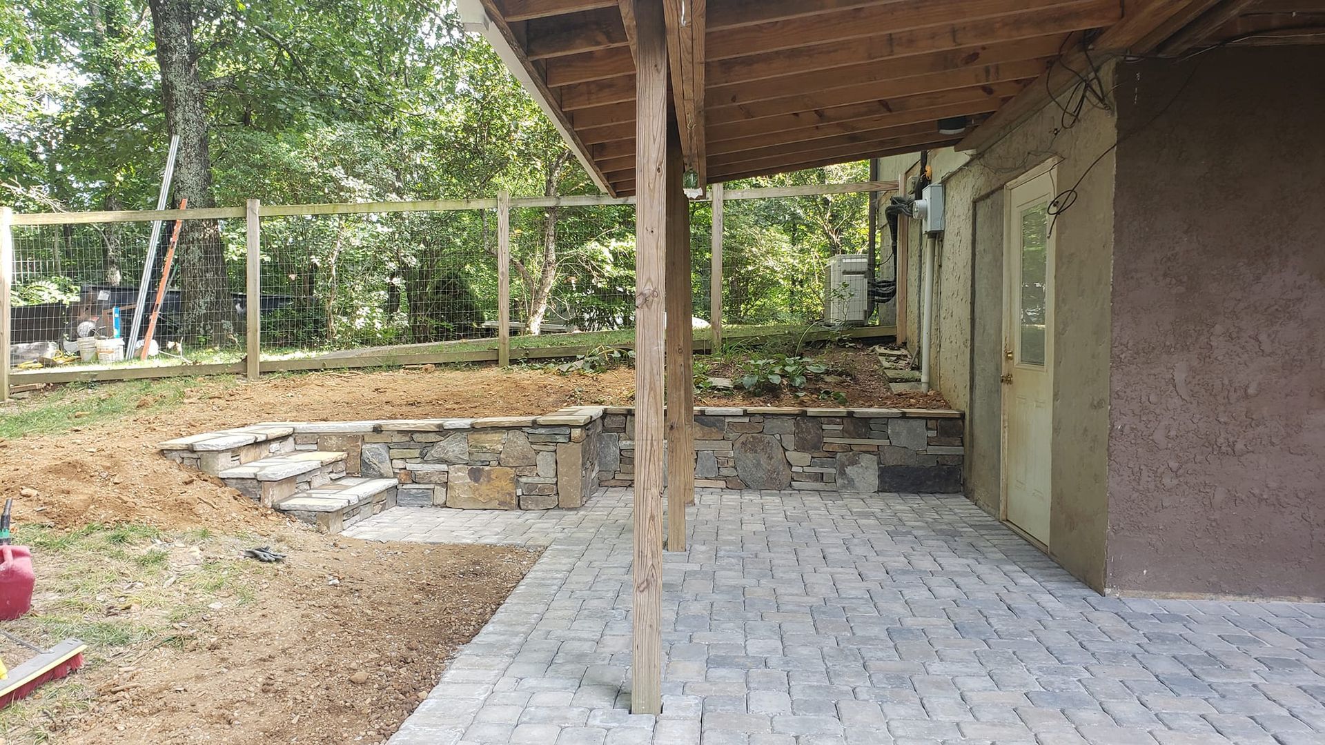 A patio with a wooden roof and a stone wall in front of a house