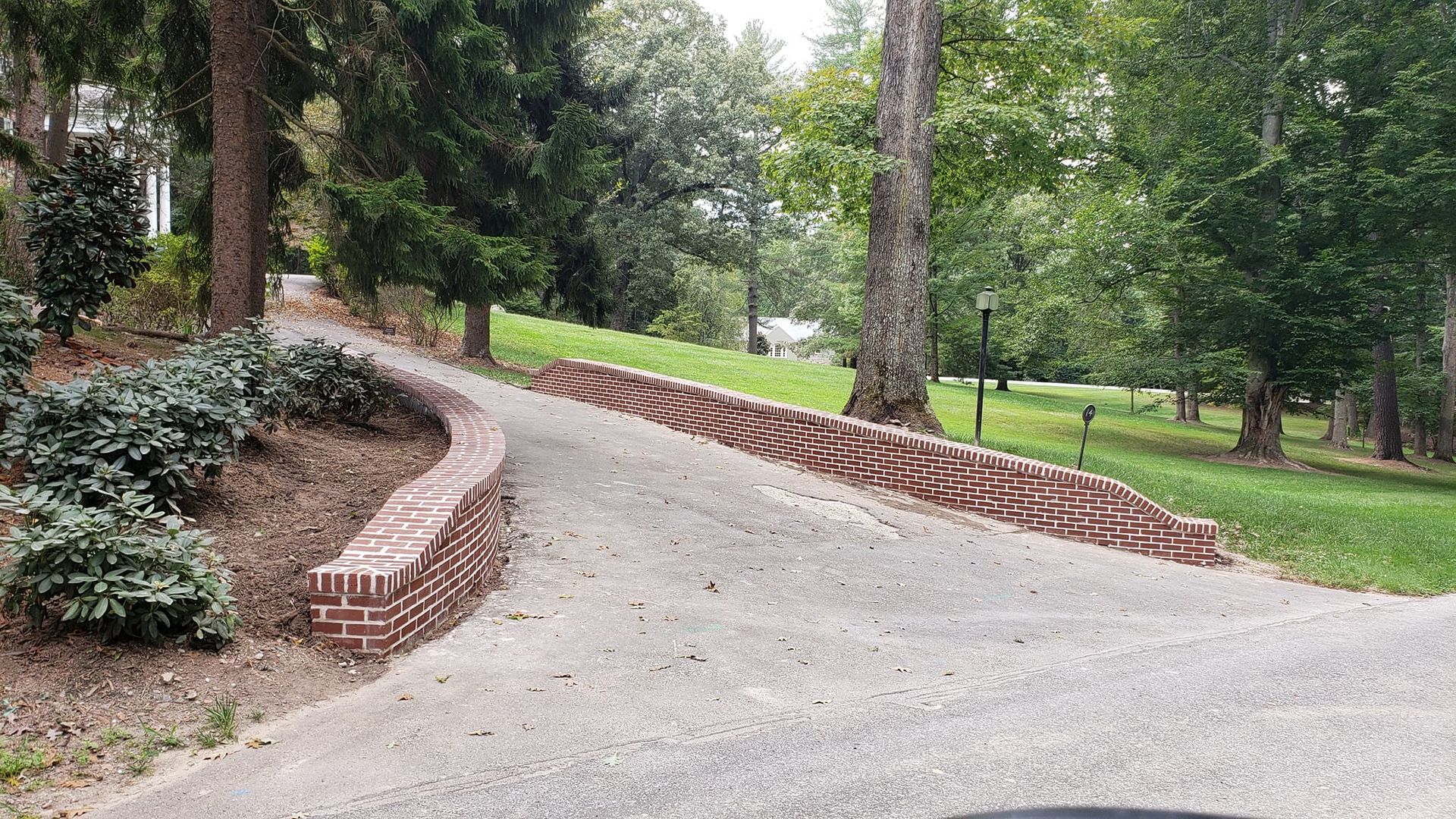 A road with a brick wall on the side of it going through a park