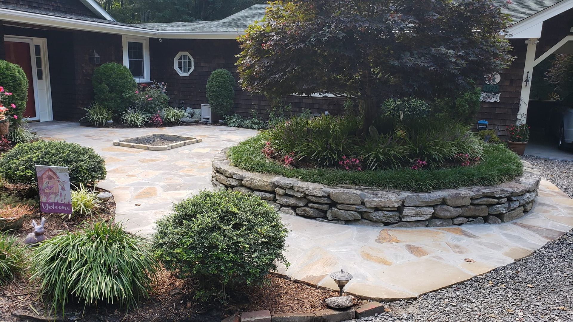 A patio with a stone wall and a tree in the middle of it in front of a house