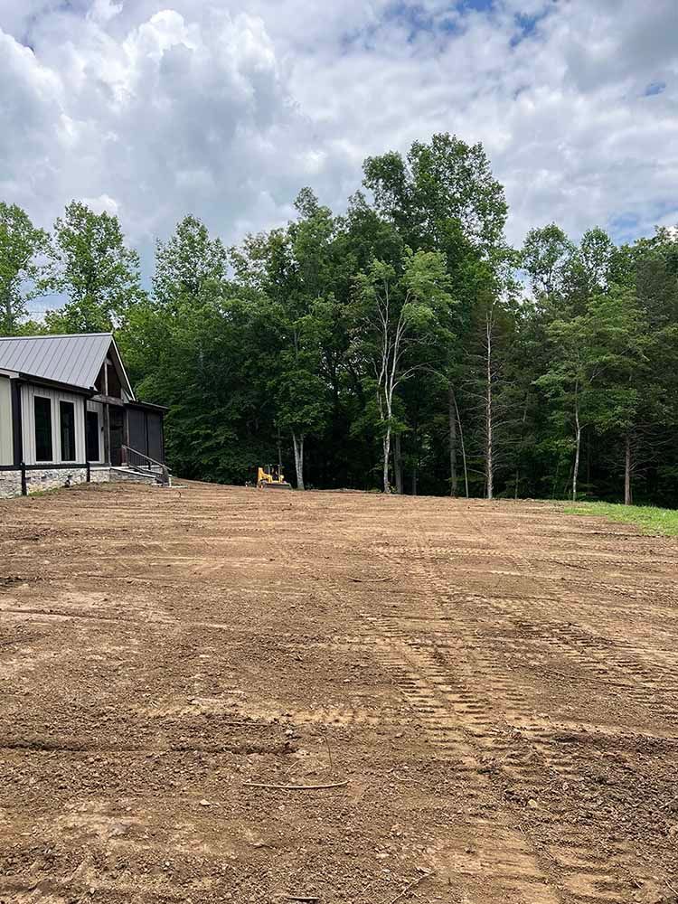 A large dirt field with a house in the background and trees in the background.