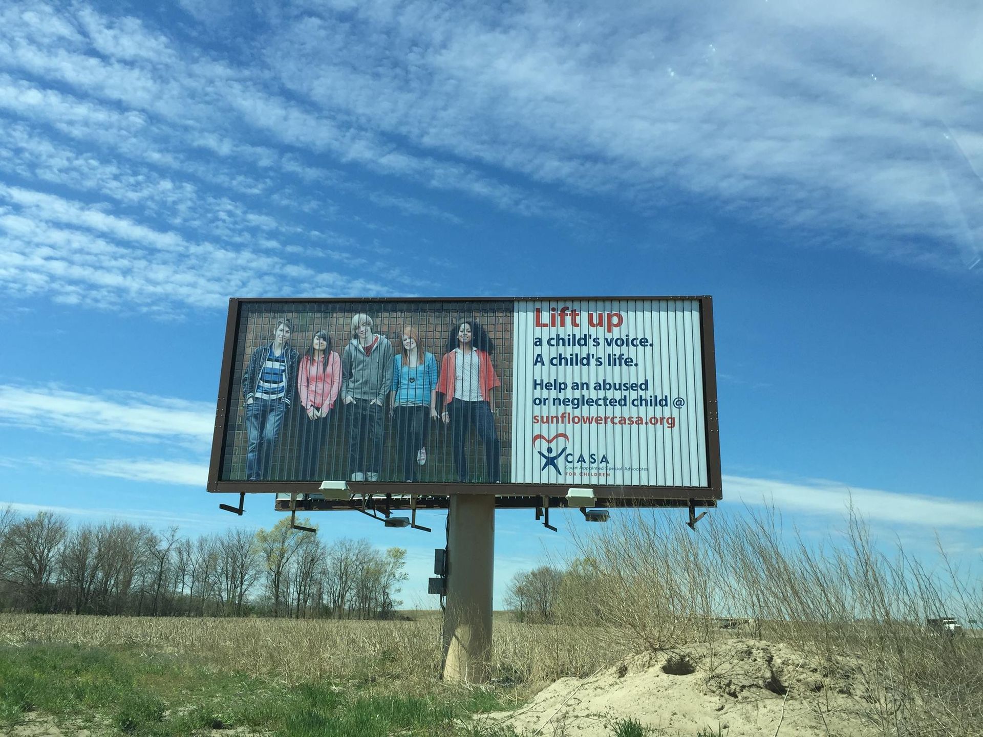 Billboard with five teens, text Lift Up, CASA Community logo, against a blue sky.