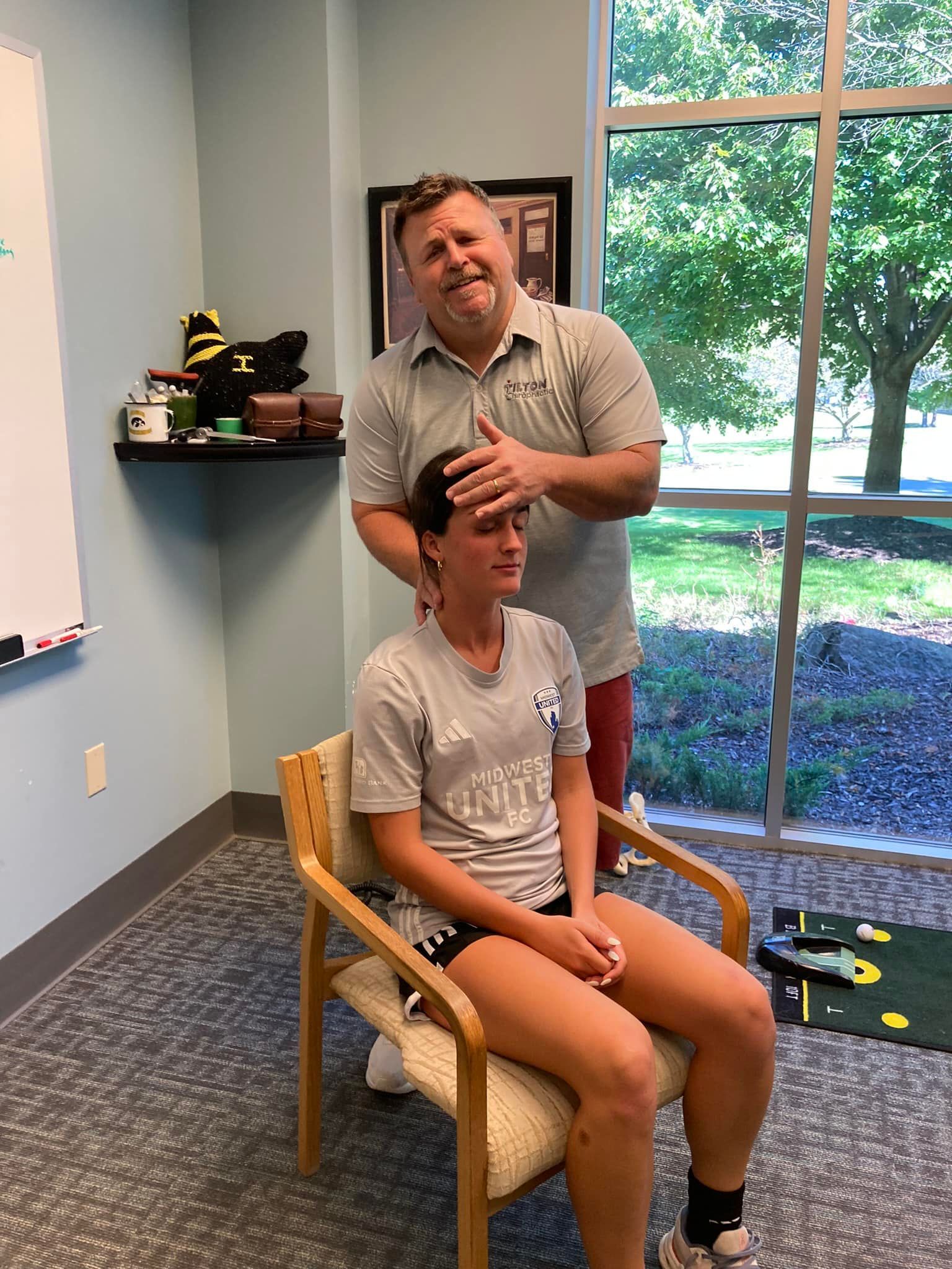 Man examining a seated person's head and neck in an office setting.
