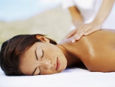 Woman receiving back massage, outdoors. Eyes closed, tan skin. Hands on her shoulder.