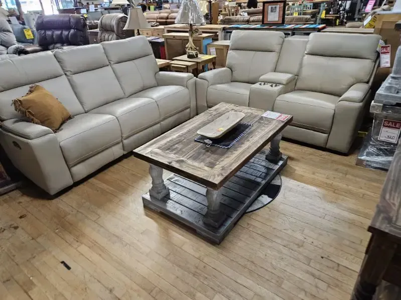 Beige reclining sofa and loveseat with a rustic coffee table on a wood floor. Inside a furniture store.