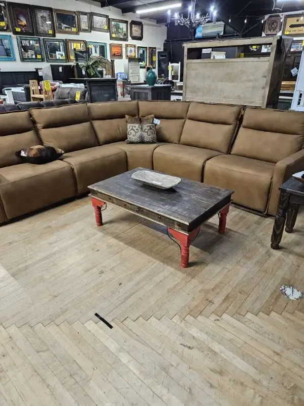 Brown sectional sofa in a furniture store, with a wooden coffee table and wood floor.