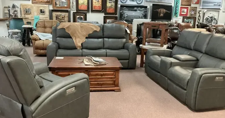 Living room furniture display: gray leather sofas, wooden coffee table, framed art on the walls.