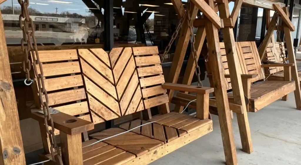 Wooden porch swings, one with a chevron back design, under a wooden structure.