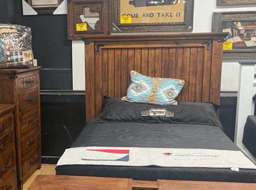 Wooden bed frame with headboard, black bedding, and decorative pillow in a furniture store.