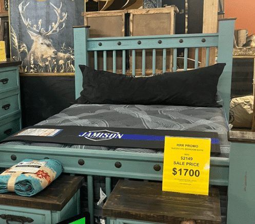 A teal bed frame with a mattress and pillow, furniture display with a price tag.