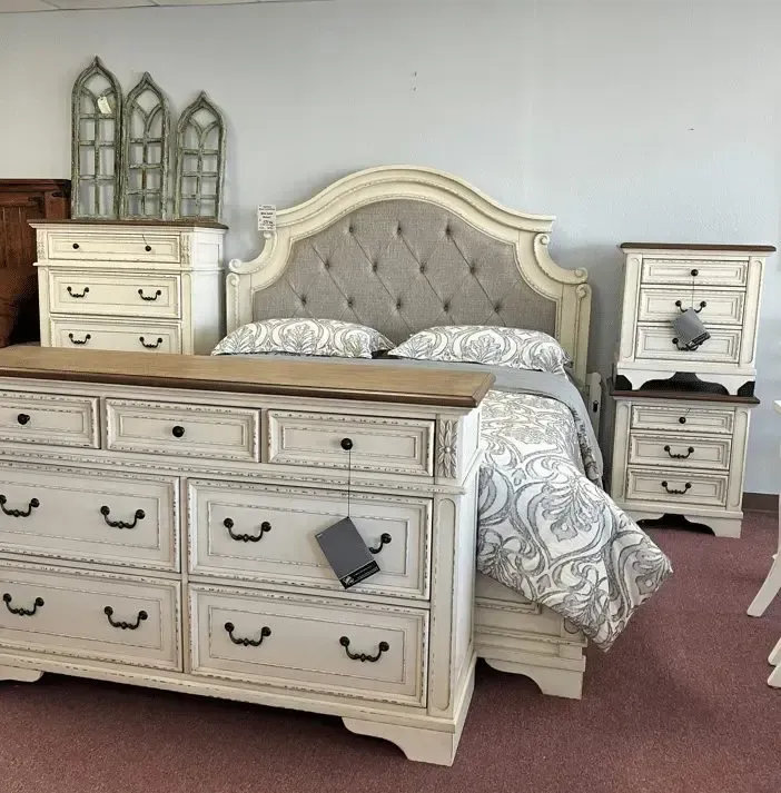 Bedroom furniture set with a tufted headboard, dresser, and nightstands, all in distressed white with a brown top.