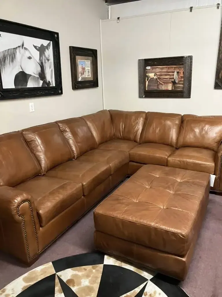 Tan leather sectional sofa with ottoman and wall art in a room.