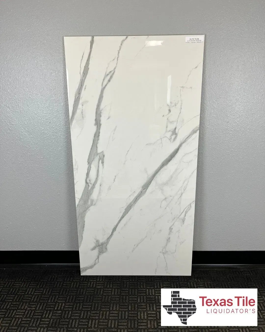 A large, glossy white rectangular tile with gray marble veining, displayed against a wall with a Texas Tile logo below.