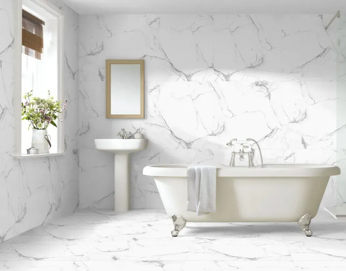 A bright, modern bathroom featuring a white clawfoot tub, a pedestal sink, and marble-patterned walls and flooring.