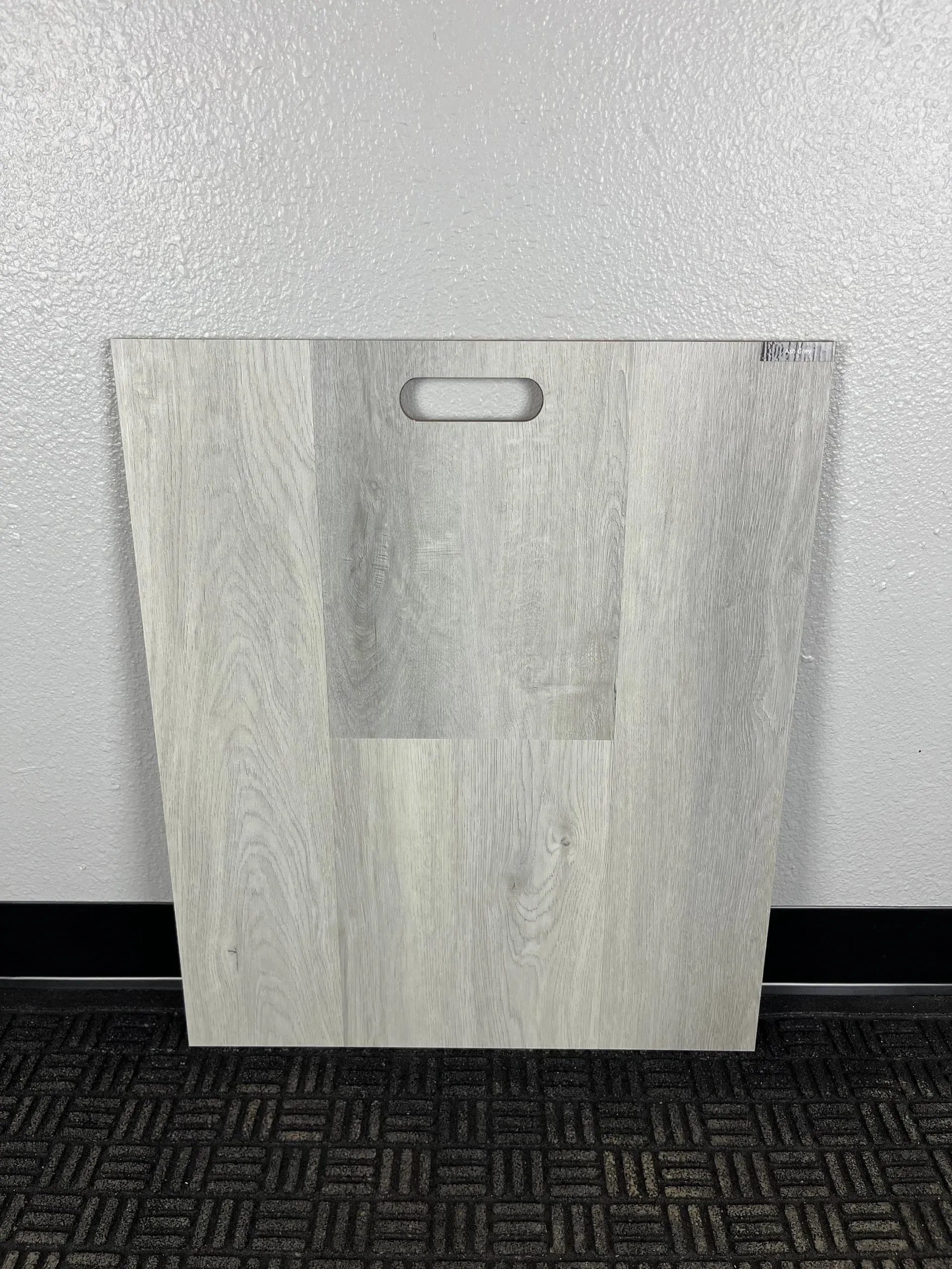 A light gray, wood-grain sample board with a cut-out handle, positioned upright against a silver-glittered wall.