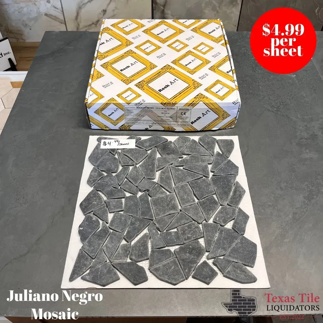 A square sheet of dark gray, irregular-shaped stone mosaic tiles sits on a table next to a patterned box.