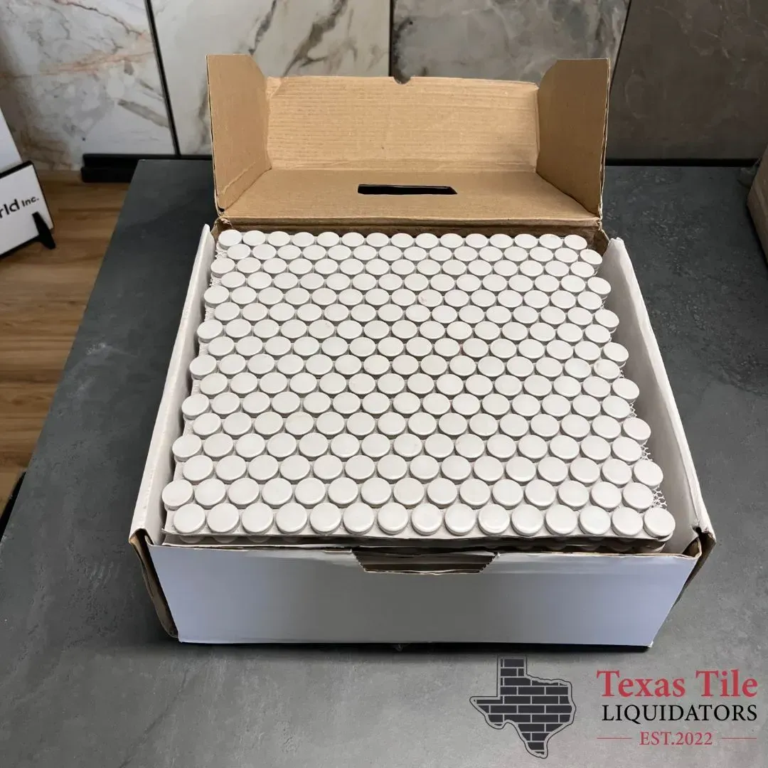 A box filled with white penny-round mosaic tiles sits on a gray surface with the Texas Tile Liquidators logo below.