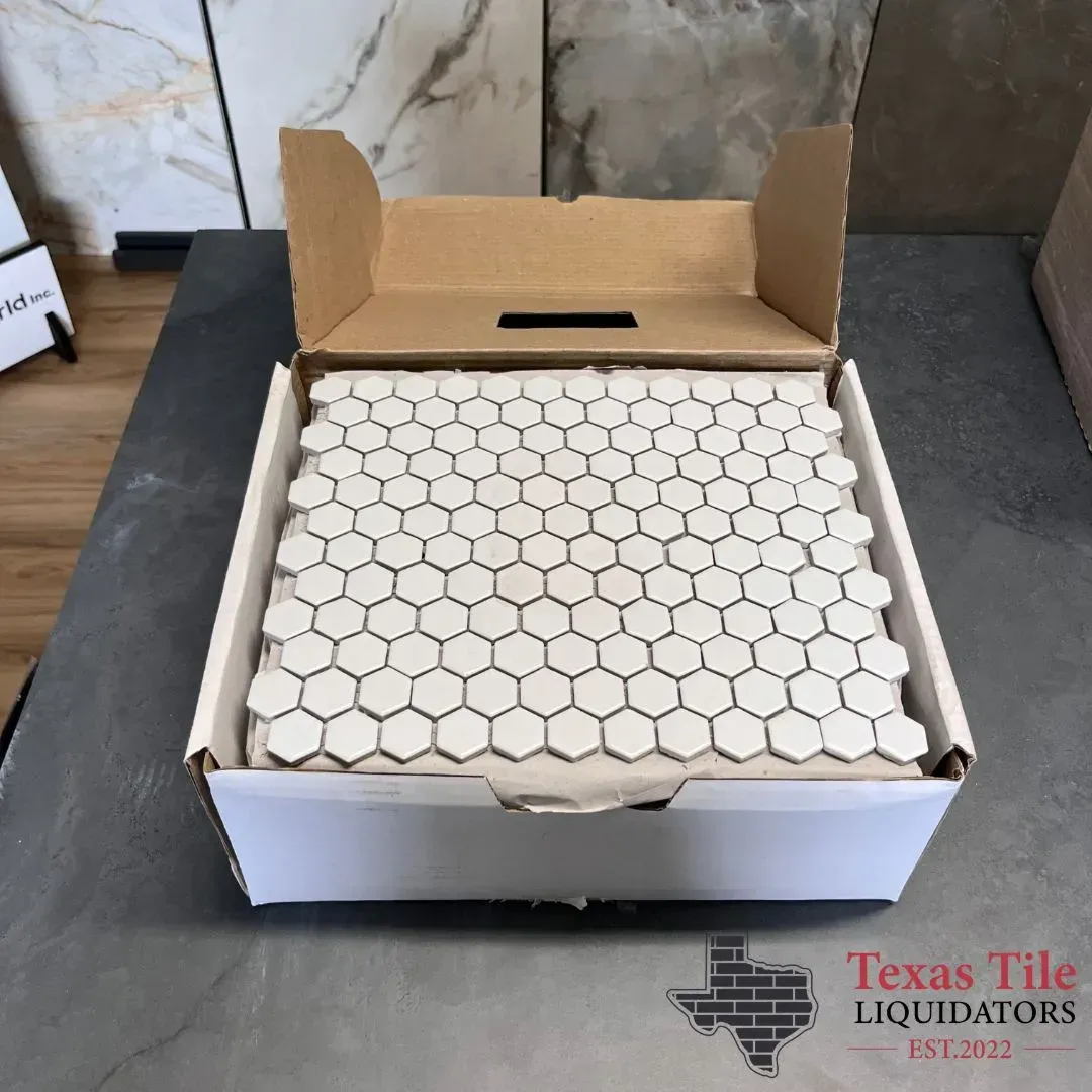 An open box containing white hexagonal mosaic tile sheets on a dark surface, with a Texas Tile Liquidators logo.