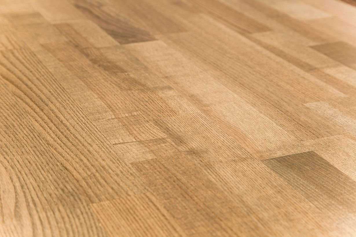 A close-up of a light brown, wooden butcher block surface with visible grain patterns and rectangular plank joints.