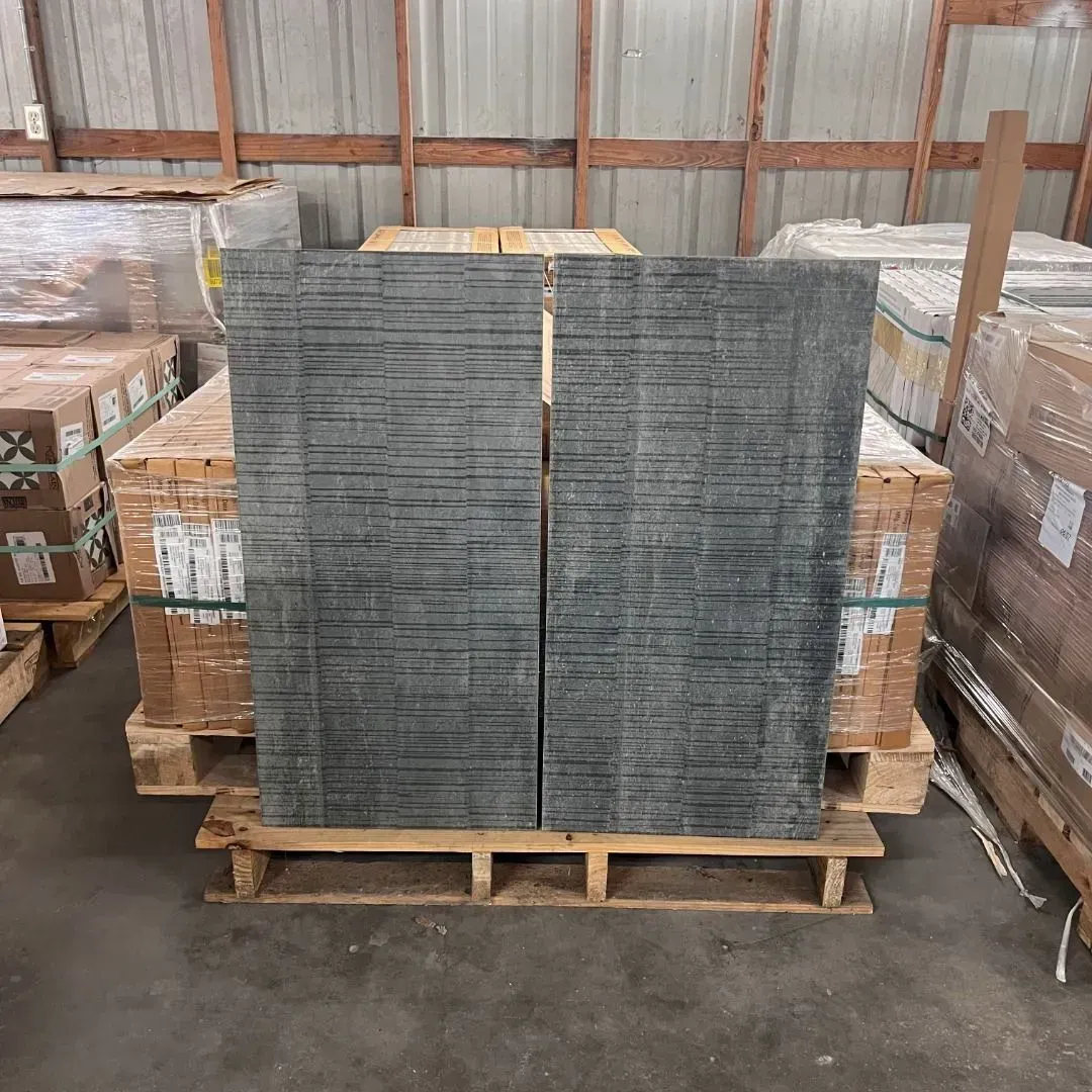 Two rectangular stone tiles with a dark grey textured, horizontal-lined pattern standing on wooden shipping pallets.