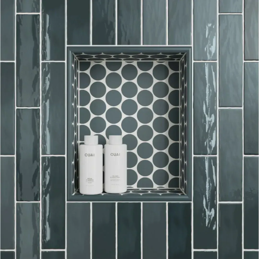 A shower niche featuring dark blue, rectangular tiles with a circular patterned back, holding two white bottles.