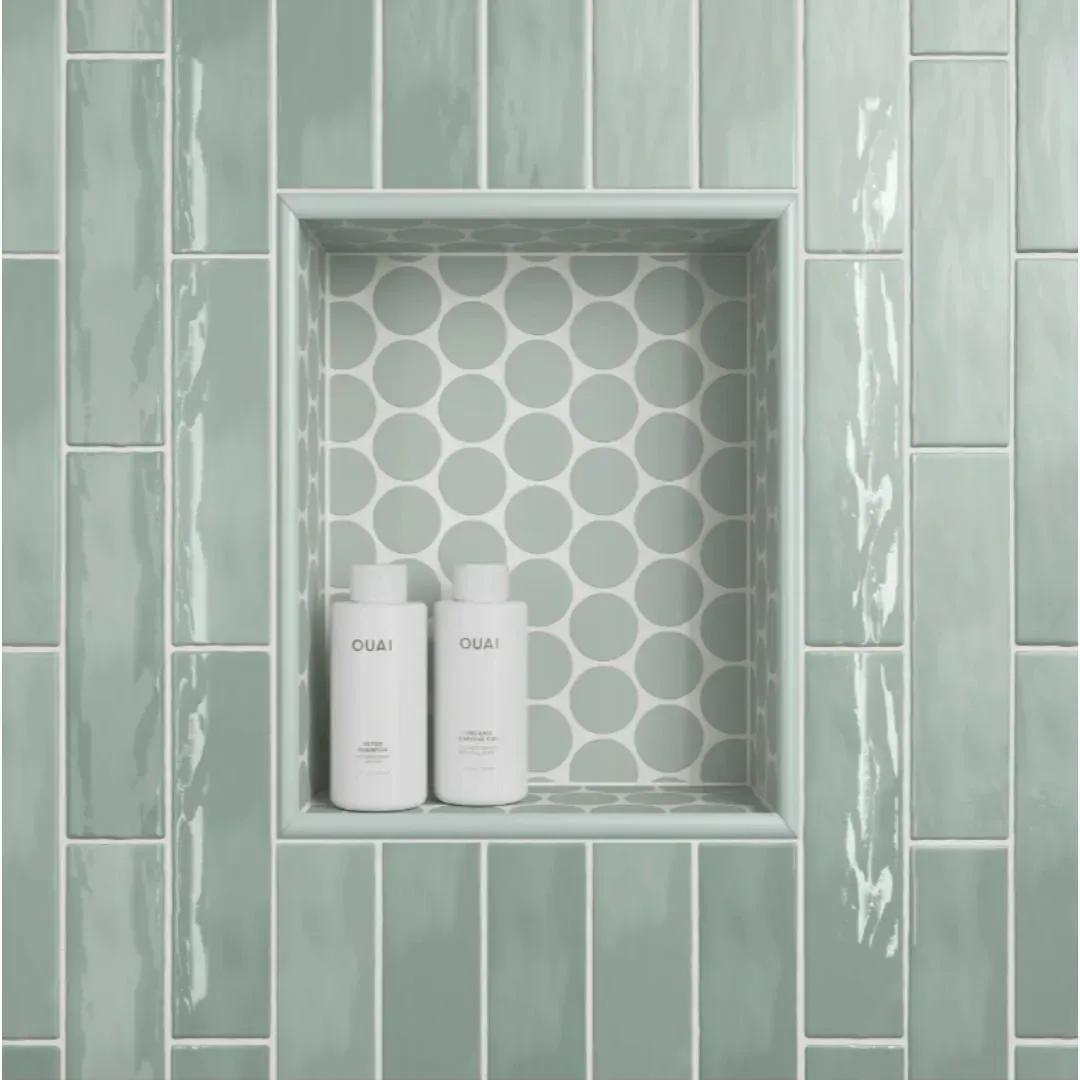 A recessed shower niche with sage green circular tiles inside, set into a wall of matching vertical rectangular tiles.