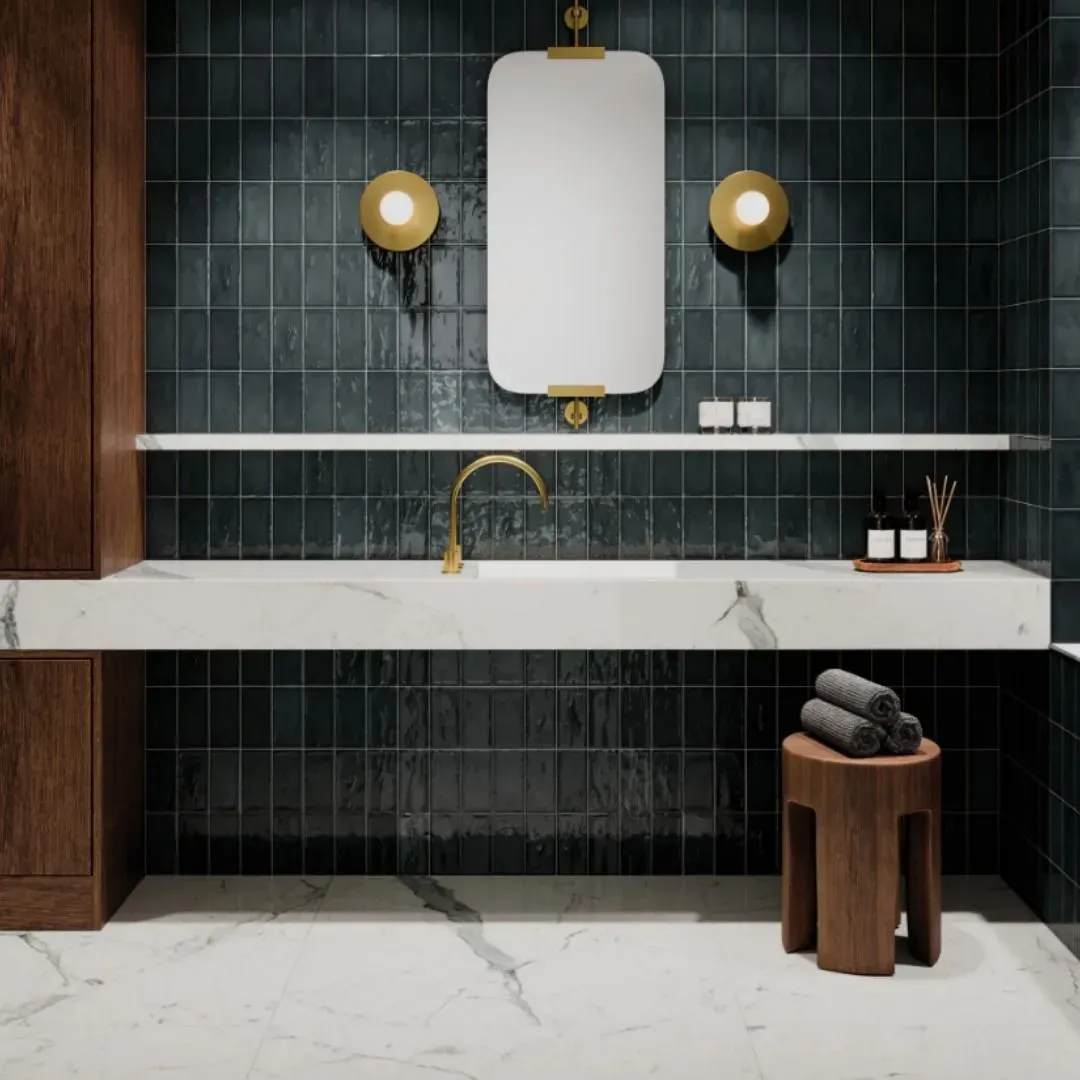 A modern bathroom vanity with a white marble countertop, gold faucet, wall mirror, and dark blue subway tile wall.