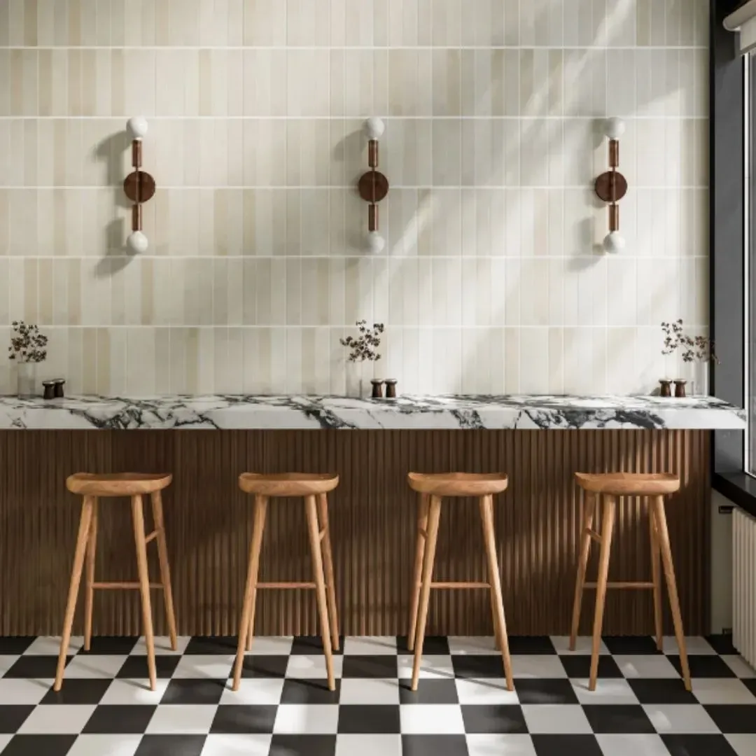A modern bar with a marble counter, wood paneling, and four wooden stools on a black and white checkered floor.