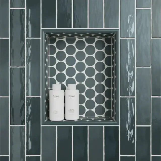 A shower niche with charcoal-colored vertical rectangular tiles and a circular patterned tile backing, holding two bottles.