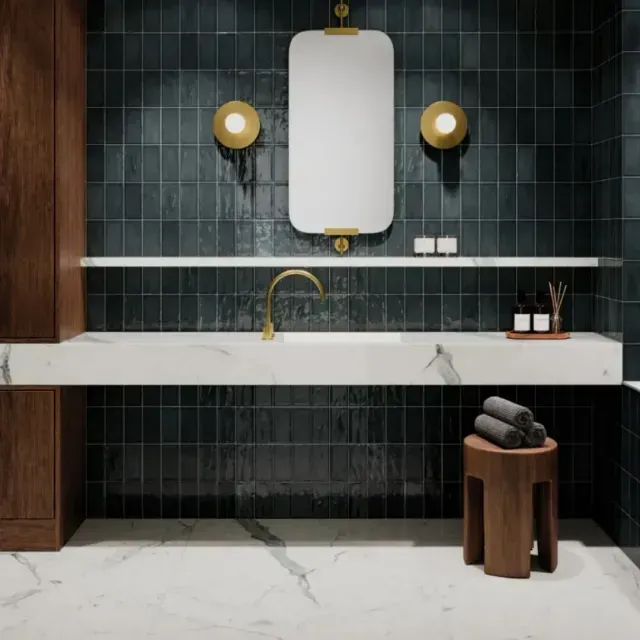 A modern bathroom vanity with a white marble countertop, gold faucet, wall mirror, and dark green tiled wall.