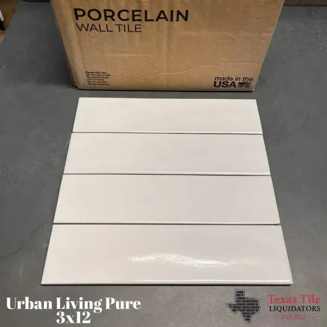 Four white 3x12 porcelain wall tiles stacked on a dark surface in front of a cardboard shipping box.