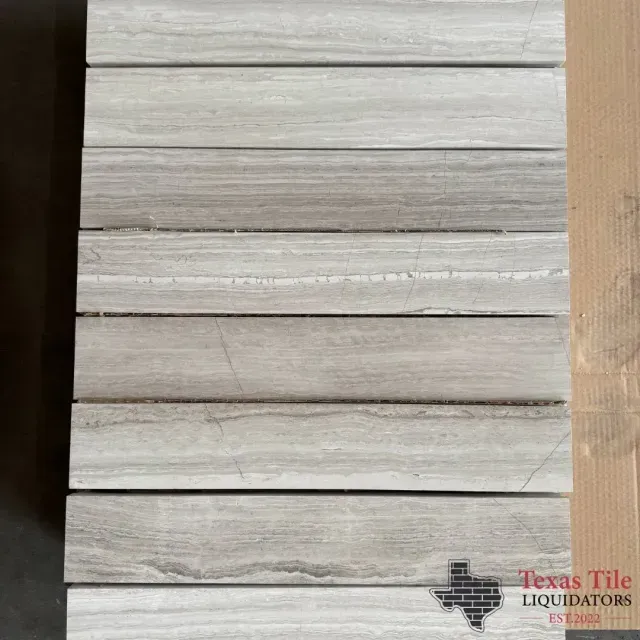 Stack of light gray wood-look porcelain tiles with horizontal grain patterns, presented by Texas Tile Liquidators.