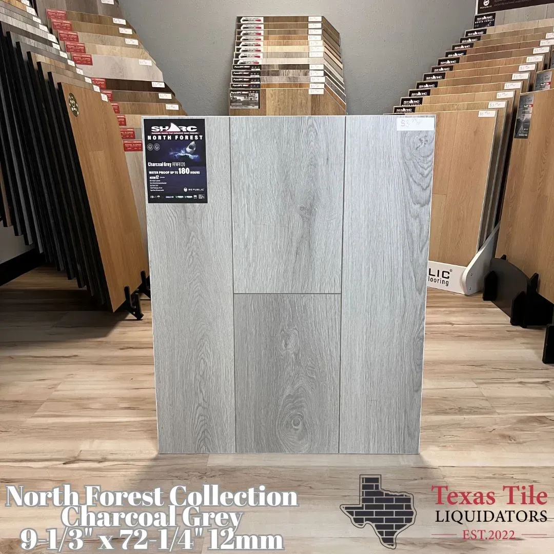 A charcoal grey wood-look flooring sample board displayed in a showroom with the Texas Tile Liquidators logo below.