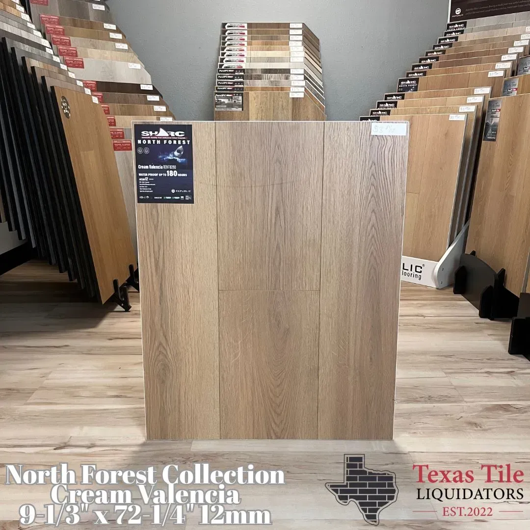 A flooring sample of light, wood-look plank in a showroom, labeled North Forest Collection Cream Valencia.