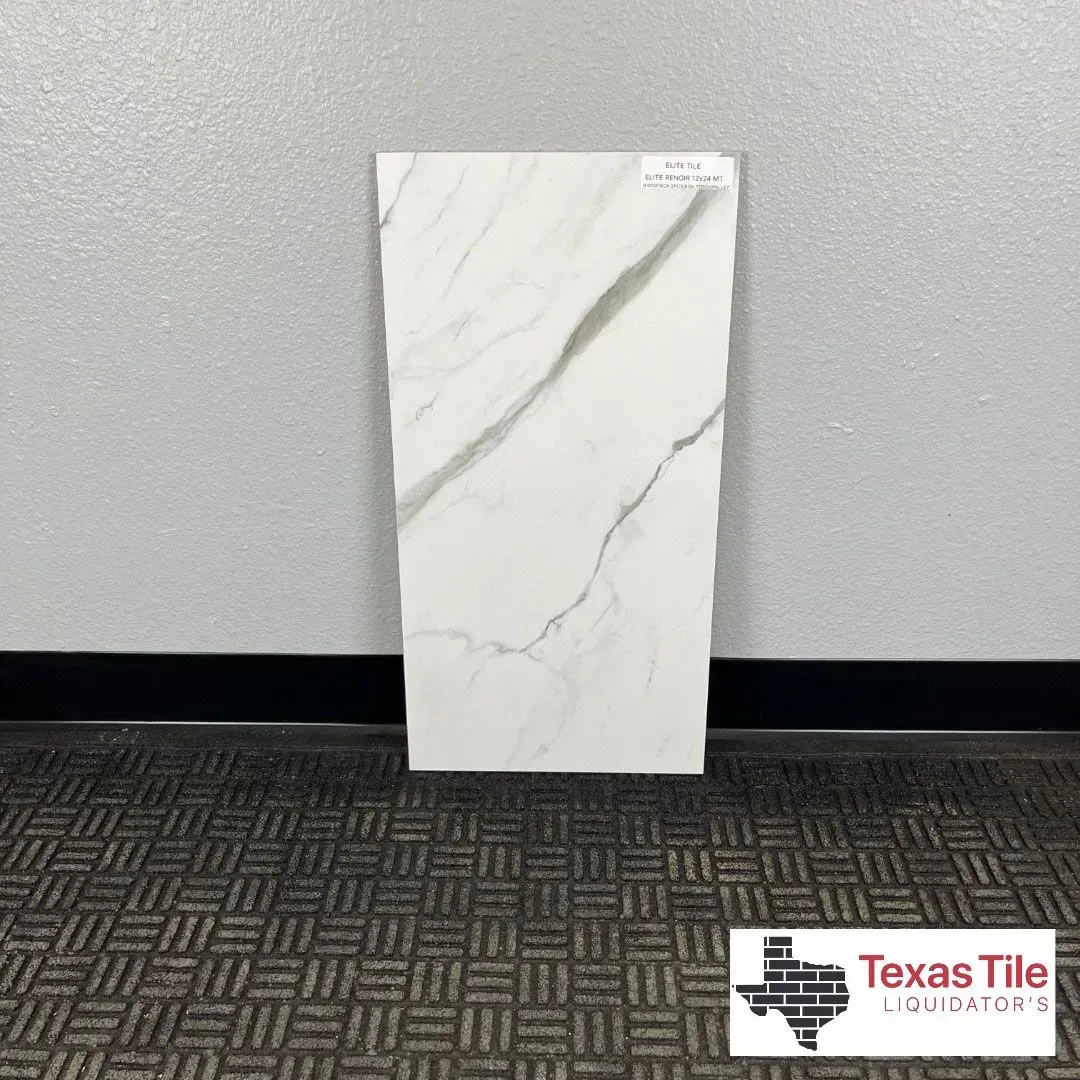 A white rectangular tile with gray marble veining stands against a gray wall above a dark patterned carpet.