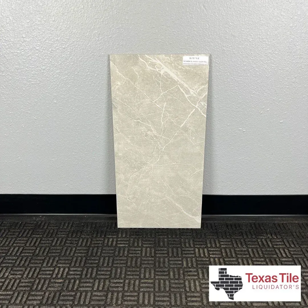 A light beige marble-look rectangular floor tile standing against a gray wall above a black rubber flooring mat.
