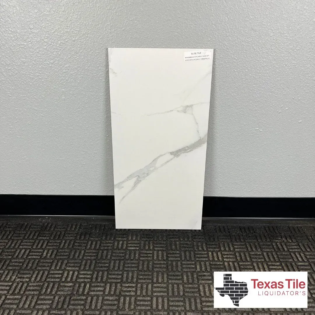 A white rectangular tile with gray marble veining stands against a gray wall above a dark patterned floor.